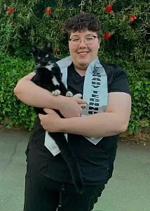 Female with short brown curly hair, wearing a sash that says Veterinary Technician and holding a black and white cat
