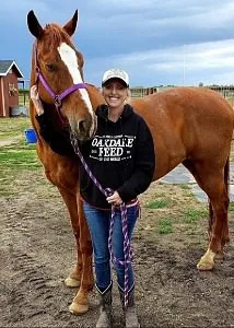Female wearing a trucker hat standing next to a brown horse with a white face